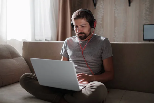 Man on sofa with headphones and notebook at home. young hipster wear headphones study online watching webinar podcast on laptop listening learning education course or music, elearning concept