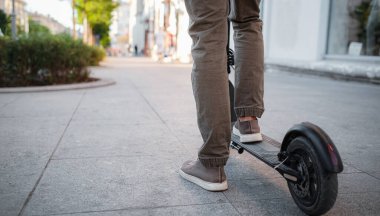Gün batımında şehir manzarasında siyah elektrikli scooter kullanan adama yakın çekim. Elektrik kentsel ulaşım konsepti resmi