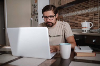 Gözlük takan, dizüstü bilgisayar kullanan, klavyeye yazan, e-posta ya da mesaj yazan, sohbet eden, alışveriş yapan, bilgisayar üzerinde çalışan, mutfakta oturan başarılı bir serbest çalışan genç adam.