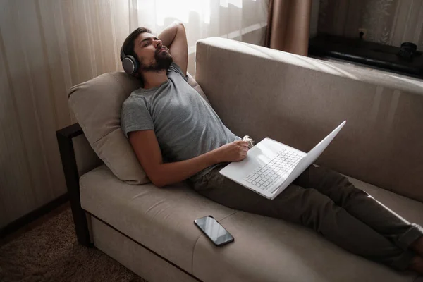 Man on sofa with headphones and notebook at home. young hipster wear headphones study online watching webinar podcast on laptop listening learning education course or music, elearning concept