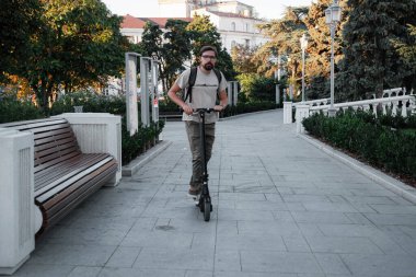 Şehrin arka planında scooter süren çekici bir adam. Şehirde elektrikli scooter sürmek eğlenceli..