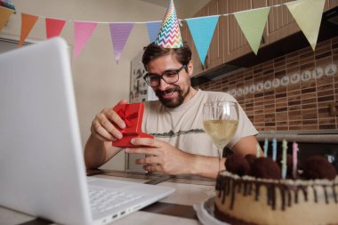 Karantina zamanında doğum gününü kutlayan bir adam. Coronavirus salgını 2020. Adam kutuyu açıyor ve hediyeyle çok mutlu oluyor. Arkadaşlarla uzaktan iletişim kurmak.