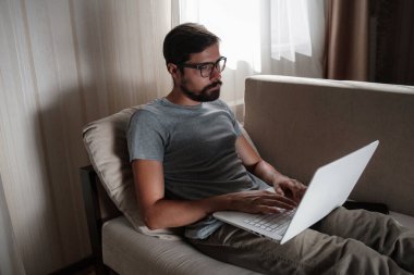 Uzaktan kumanda. Dizüstü bilgisayarda çalışan bir adam evdeki koltukta oturuyor. Metin için Boşluğu Kopyala. Serbest çalışan hipster, ortaklarıyla çalışır, çalışır ya da iletişim kurar.