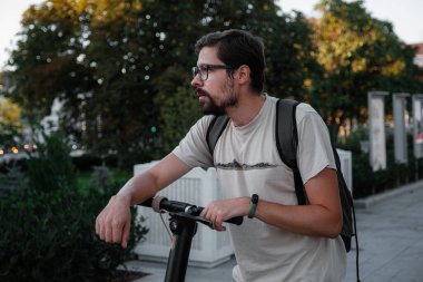 Şehrin arka planında scooter süren çekici bir adam. Şehirde elektrikli scooter sürmek eğlenceli..