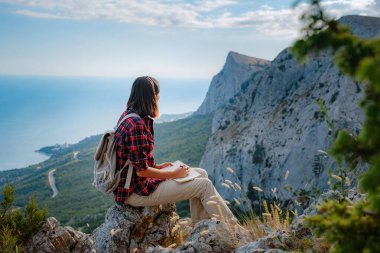 Kadın yürüyüşçü dağ tepesi manzarasının tadını çıkarıyor not defterine fikirler yazıyor. Eko-turizm seyahati. Keşif Seyahat Hedefi Konsepti