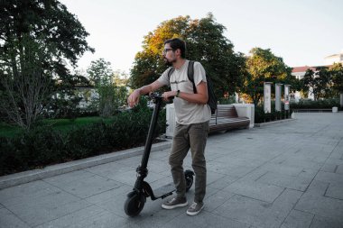 Şehrin arka planında scooter süren çekici bir adam. Şehirde elektrikli scooter sürmek eğlenceli..