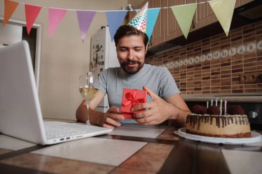 Karantina zamanında doğum gününü kutlayan bir adam. Coronavirus salgını 2020. Adam kutuyu açıyor ve hediyeyle çok mutlu oluyor. Arkadaşlarla uzaktan iletişim kurmak.