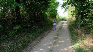 Kırsal alanlarda yürüyüş yapan bir kadın, açık araziler, temiz hava ve huzurlu kırsal manzarayla çevrili. Açık havanın doğal güzelliğini ve sükunetini seviyor..