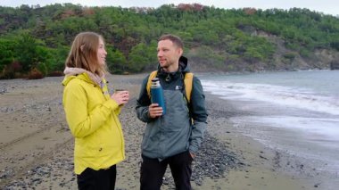 Genç çift kışın deniz kenarında çay içer. Bulutlu gökyüzü, hafif rüzgar, soğuk hava, sıcak içecekler. Sakin sakin bir an, günlük hayattan rahat bir kaçış, doğada derin bir bağ..