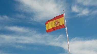 İspanyol bayrağı zarif bir şekilde mavi gökyüzüne doğru dalgalanıyor. Spains kültürel kimliğinin özünü yakalayan ulusal gurur, birlik ve mirasın güçlü bir sembolü.