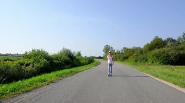 Güneşli bir günde asfalt yolda yürüyen bir kadın yürüyüş macerasına girişiyor. Manzaralı manzaralar ve açık hava ile çevrelenmiş, seyahatin ve açık hava deneyiminin tadını çıkarıyor..