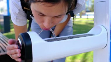 Genç bir kadın Abu Dabi 'deki parktaki bir çeşmeden su içiyor. Palmiye ağaçları ve yeşilliklerle çevrili. Sakin bir vahada güneşli bir günde ferahlatıcı bir an..
