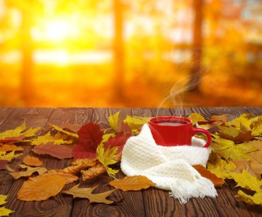Sonbahar yaprakları ve sıcak bir fincan kahve. Güneş ışığı arka planında tahta masa. Sonbahar zaman kavramı.