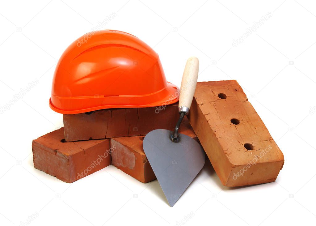 Brick, red hard hat and tools isolated on white background