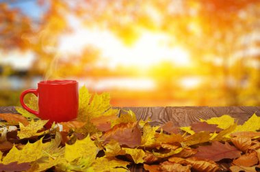 Sonbahar yaprakları ve sıcak bir fincan kahve. Güneş ışığı arka planında tahta masa. Sonbahar zaman kavramı.
