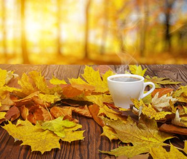 Sonbahar yaprakları ve sıcak bir fincan kahve. Güneş ışığı arka planında tahta masa. Sonbahar zaman kavramı.