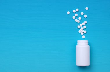 Çeşitli ilaç hapları, haplar, kapsüller ve mavi arka planda beyaz şişe. Uzayı metin için kopyala. Düz yatıyordu. Üst görünüm