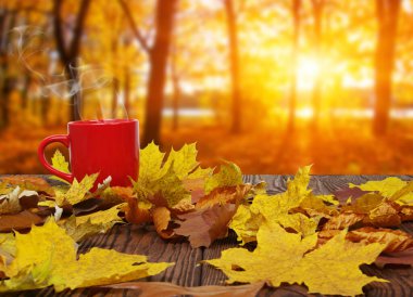 Sonbahar yaprakları ve sıcak bir fincan kahve. Güneş ışığı arka planında tahta masa. Sonbahar zaman kavramı.