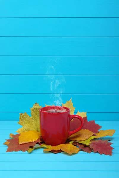 Autumn leaves, hot steaming cup of coffee  on wooden blue background.