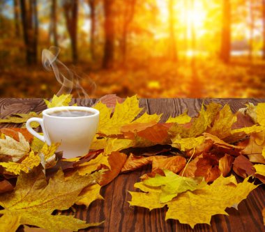 Sonbahar yaprakları ve sıcak bir fincan kahve. Güneş ışığı arka planında tahta masa. Sonbahar zaman kavramı.