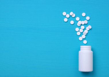 Mavi arka planda beyaz şişeden dökülen haplar. Kopyalama alanı olan üst görünüm. Tıp konsepti