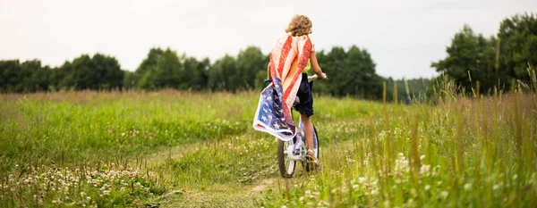 Symbole de célébration 4 quatrième de juillet. Jeune fille à vélo avec drapeau américain à la main — Photo