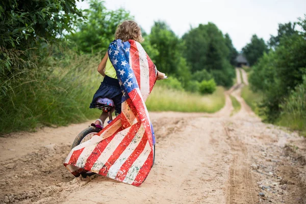 Symbol of celebration 4 fourth of july. Young Girl riding bicycle with american flag in hand — Stock Photo, Image