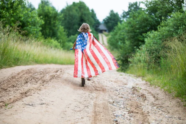 Simbolo di celebrazione 4 4 luglio. Giovane ragazza in bicicletta con bandiera americana in mano — Foto Stock