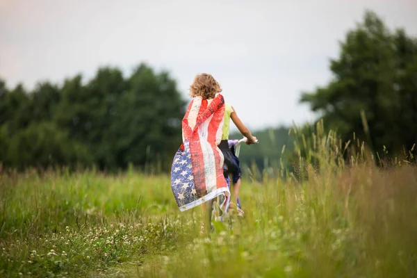 7月4日のお祝いのシンボル。アメリカ国旗を手に自転車に乗る少女 — ストック写真