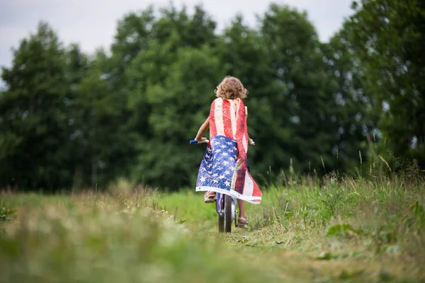 Symbol of celebration 4 fourth of july. Young Girl riding bicycle with american flag in hand — Stock Photo, Image
