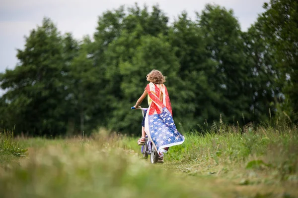 Symbol of celebration 4 fourth of july. Young Girl riding bicycle with american flag in hand — Stock Photo, Image