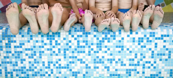 Group of people legs while sitting on edge of swimming pool. Feet of group of friends or parents with children on edge of swimming pool