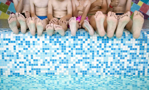 Group of people legs while sitting on edge of swimming pool. Feet of group of friends or parents with children on edge of swimming pool