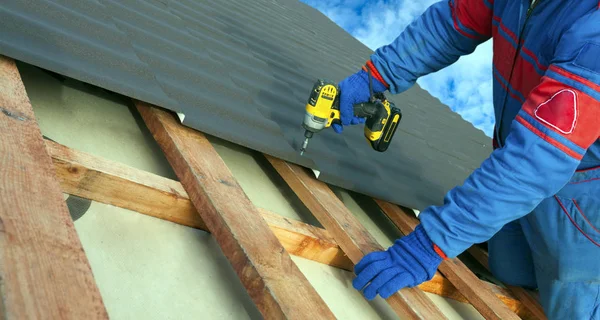 人の労働者はネジでキャップ金属屋根の仕事を取り付けるためにパワードリルを使用します — ストック写真