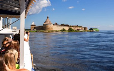 Shlisselburg, Russia - August 8, 2018: River cruise ship sailing on the Neva river to historical fortress Oreshek in summer sunny day clipart