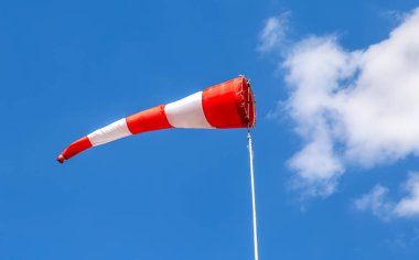Mavi gökyüzüne karşı kırmızı ve beyaz çizgilerle uçan rüzgar gülü