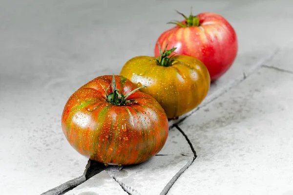 Heirloom tomatoes. Three tomatoes of different colors on a gray concrete table with a crack.