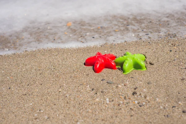 Red and green starfish-shaped molds on the sand — Stock Photo, Image