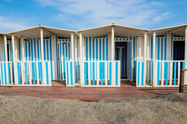 Randig vit och blå randig strandhus och svart sandstrand. — Stockfoto