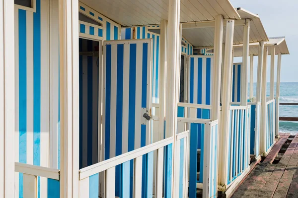 Gestreifte weiß und blau gestreifte Strandhäuser und schwarzer Sandstrand. — Stockfoto