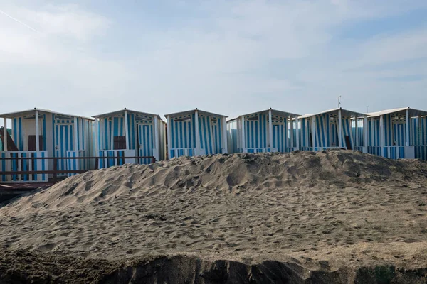 Pasiaste białe i niebieskie pasiaste domy plażowe i czarna piaszczysta plaża. — Zdjęcie stockowe