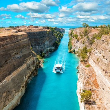 Parlak güneşli bir günde beyaz bulutlar ile mavi gökyüzü karşı Korint kanalı güzel sahne. Beyaz gemi turkuaz suda yüzen kayaların arasında. 