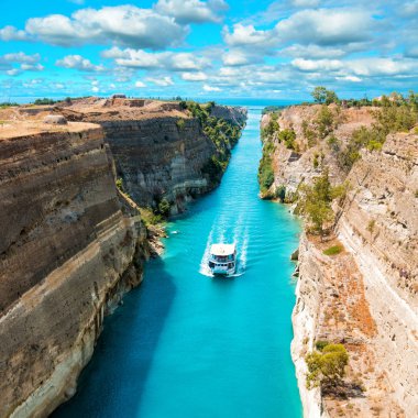Beautiful scenery of the Corinth Canal in a bright sunny day against a blue sky with white clouds. Among the rocks floating white ship in turquoise water.  clipart