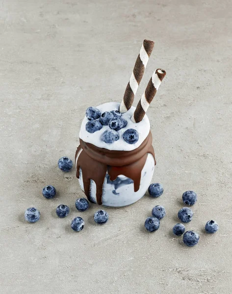 dessert of frozen banana, icecream and blueberries in a jar decorated with melted chocolate