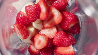 Sağlıklı kahvaltı içeceği, üst manzara, yavaş çekim için blender 'a çilek ve muz parçaları dökülüyor.