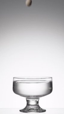 Şeffaf sıvı bardaktan dökülen zeytinler sıçrama yapar.