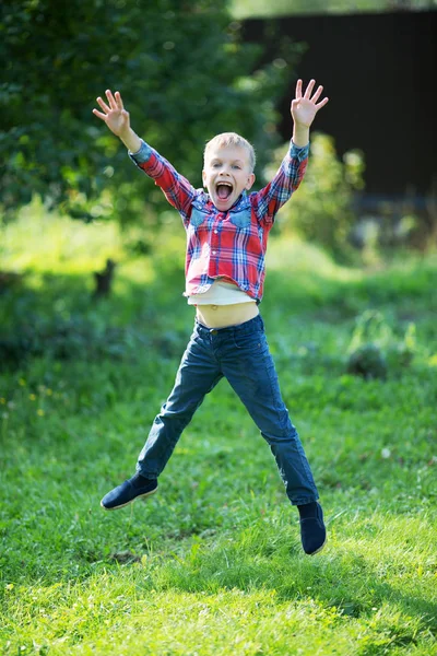 Küçük çocuk sevinçle yaz aylarında bahçede atlama — Stok fotoğraf