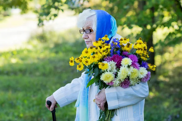 Бабушка с тростью и цветами на фоне деревьев — стоковое фото