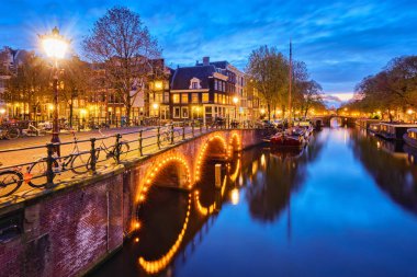 Alacakaranlıkta, Kanal, köprü ve ortaçağ evleriyle Amterdam şehir manzarası aydınlandı. Amsterdam, Hollanda