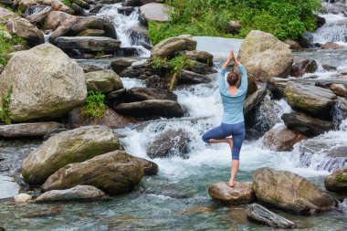 Yogadaki kadın, Vrikshasana ağacı, şelalede poz veriyor.